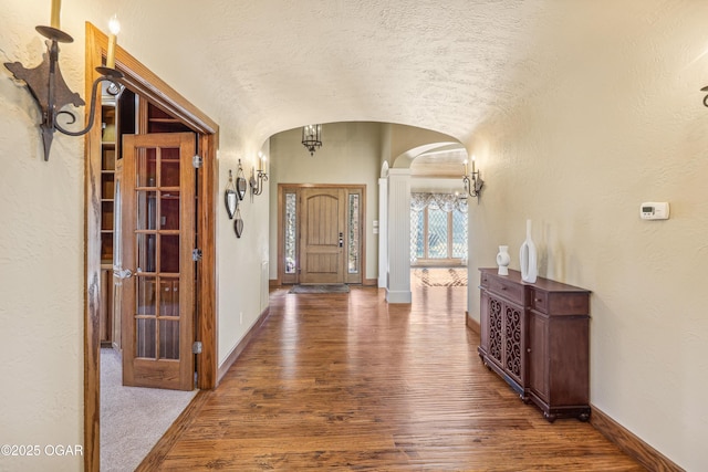 foyer entrance with baseboards, arched walkways, wood finished floors, and vaulted ceiling