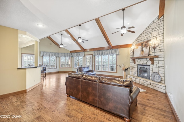 living area with ceiling fan, plenty of natural light, a stone fireplace, and wood finished floors