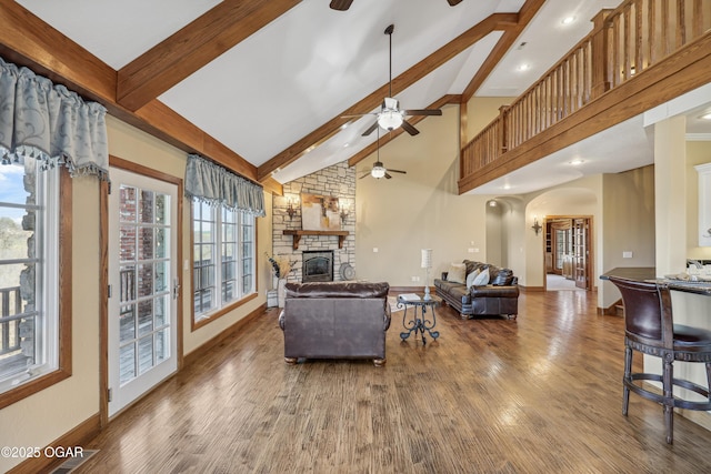 living room featuring beamed ceiling, wood finished floors, arched walkways, a fireplace, and ceiling fan