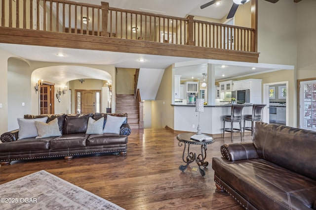 living area with arched walkways, a towering ceiling, a ceiling fan, and wood finished floors