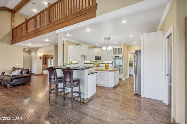 kitchen featuring wood finished floors, open floor plan, arched walkways, appliances with stainless steel finishes, and white cabinets