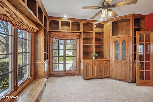 unfurnished office featuring built in shelves, light colored carpet, and ceiling fan