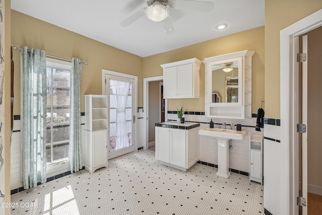 kitchen featuring dark countertops, a wainscoted wall, ceiling fan, white cabinetry, and tile walls