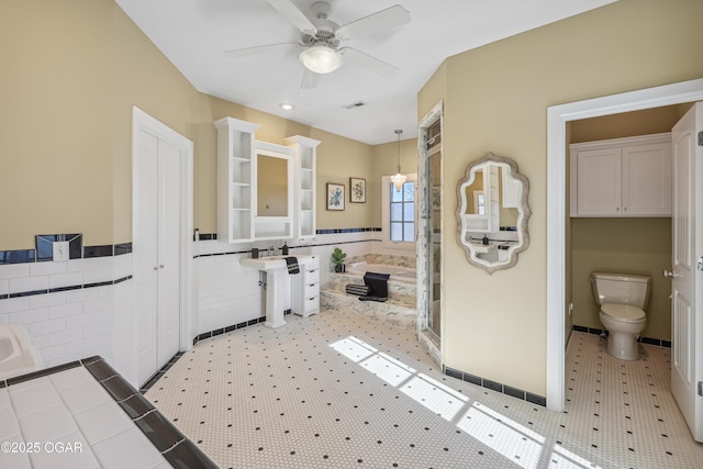 full bathroom with visible vents, ceiling fan, toilet, a bath, and tile walls