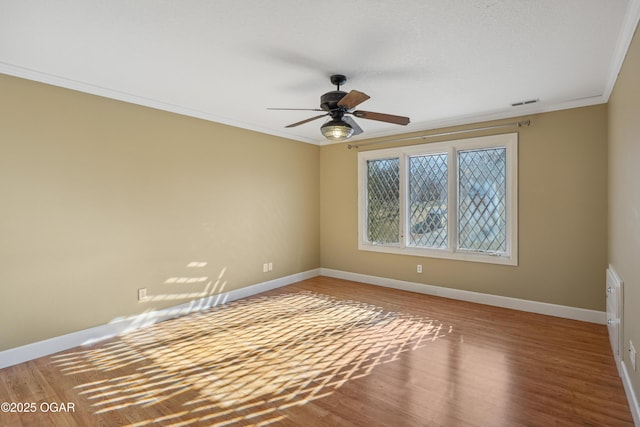 spare room with visible vents, ornamental molding, wood finished floors, baseboards, and ceiling fan