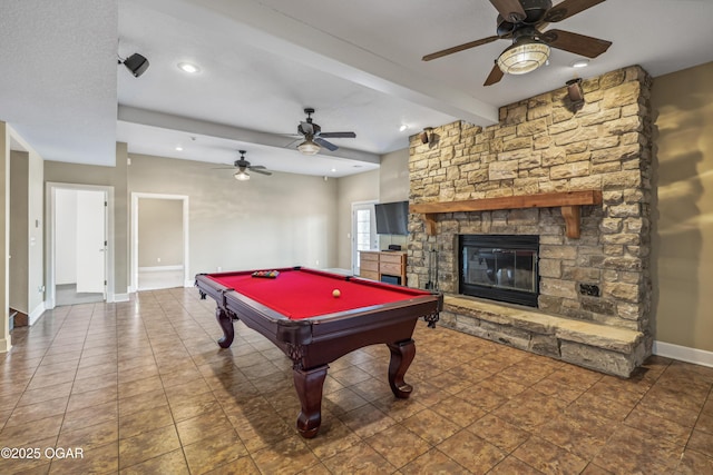 recreation room with beam ceiling, baseboards, a stone fireplace, and a ceiling fan