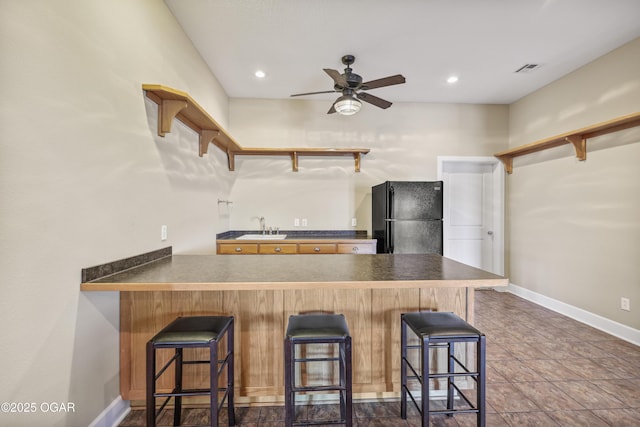 kitchen featuring open shelves, ceiling fan, a peninsula, freestanding refrigerator, and a sink