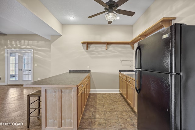 kitchen featuring a breakfast bar, open shelves, freestanding refrigerator, ceiling fan, and dark countertops