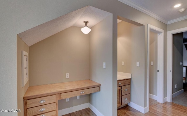 unfurnished office featuring built in desk, baseboards, light wood-style floors, and ornamental molding