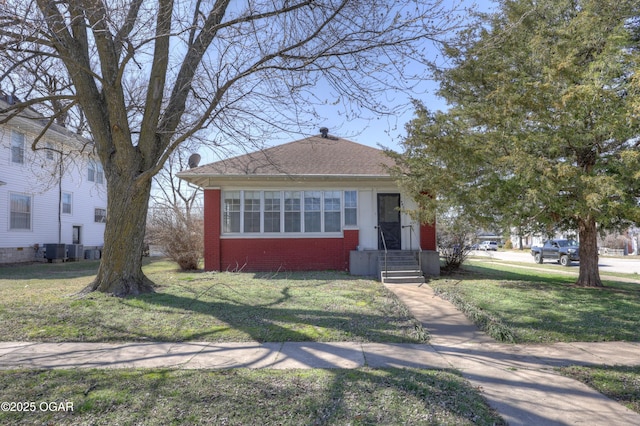 bungalow with a front yard, central air condition unit, brick siding, and a chimney