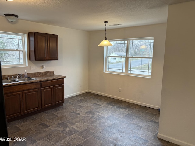 kitchen featuring baseboards, visible vents, a sink, stone finish flooring, and dark countertops