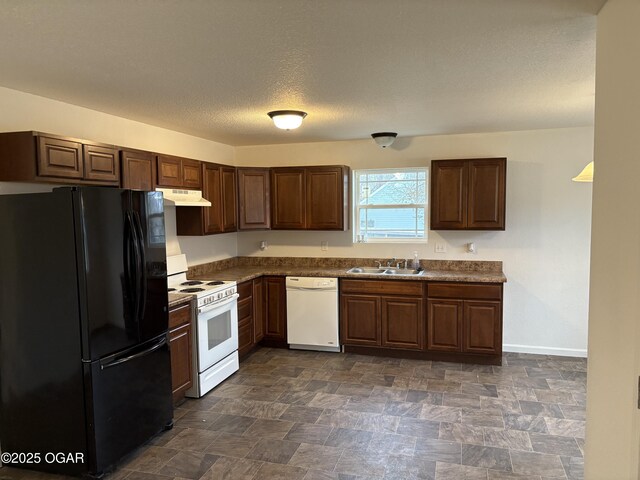 kitchen with under cabinet range hood, stone finish flooring, dark countertops, white appliances, and baseboards