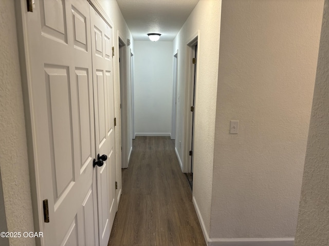 hallway with dark wood-style floors, baseboards, and a textured wall