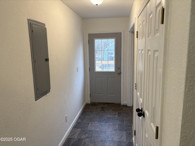 doorway to outside featuring stone finish flooring, baseboards, electric panel, a textured wall, and a textured ceiling