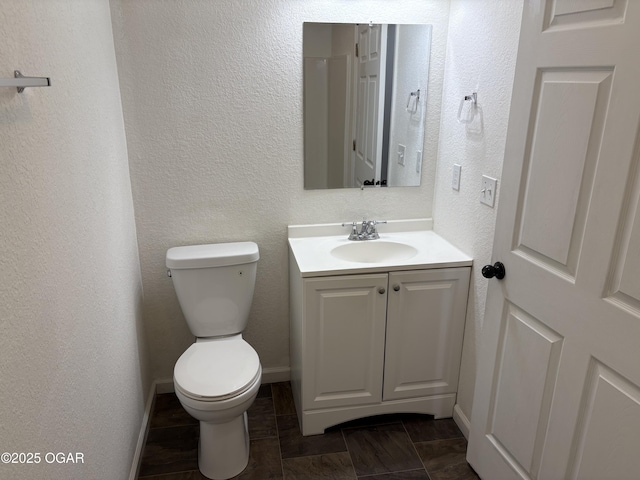 bathroom featuring vanity, toilet, a textured wall, and baseboards