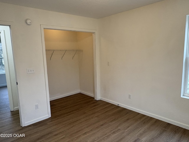 unfurnished bedroom featuring dark wood-style floors, a closet, and baseboards