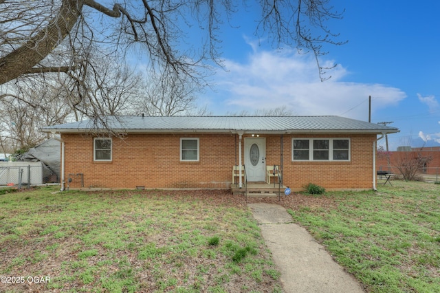 single story home featuring brick siding, metal roof, a front lawn, and fence