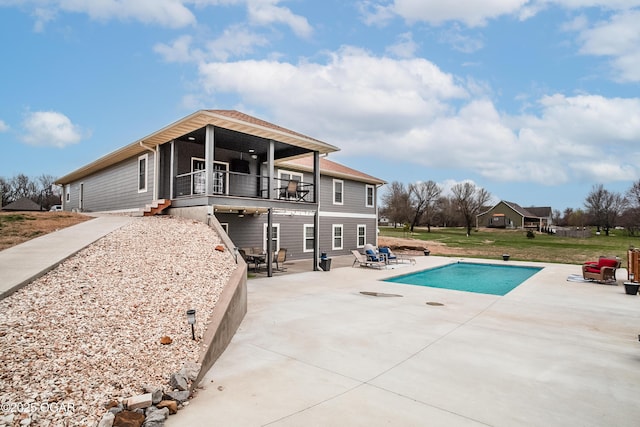 rear view of property featuring a patio area, a lawn, an outdoor pool, and a balcony