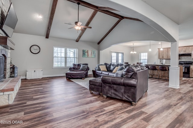living area with beamed ceiling, ceiling fan with notable chandelier, a fireplace, wood finished floors, and arched walkways