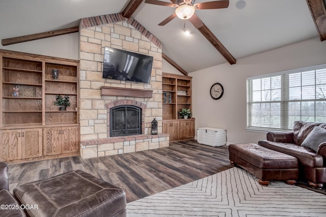 living area with lofted ceiling with beams, wood finished floors, a stone fireplace, and ceiling fan