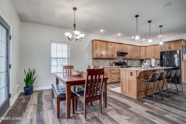 kitchen with a notable chandelier, under cabinet range hood, dark wood finished floors, decorative backsplash, and black refrigerator with ice dispenser