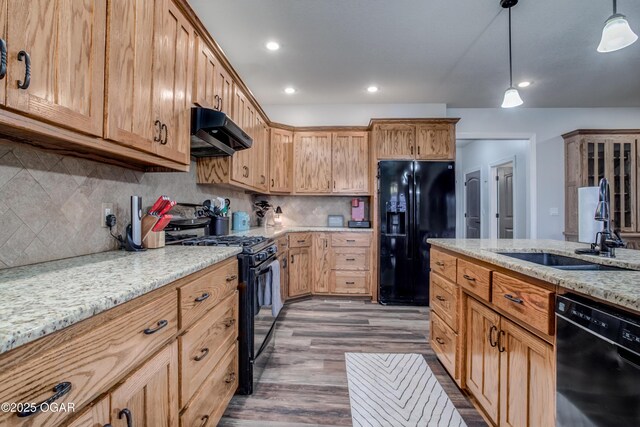 kitchen featuring light stone countertops, a sink, black appliances, extractor fan, and pendant lighting