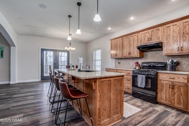 kitchen with a breakfast bar area, dark wood-style floors, black gas range, under cabinet range hood, and tasteful backsplash