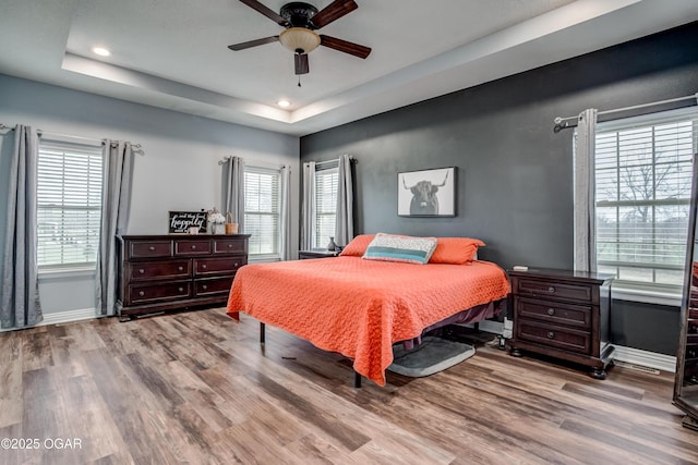 bedroom featuring baseboards, recessed lighting, wood finished floors, a raised ceiling, and a ceiling fan