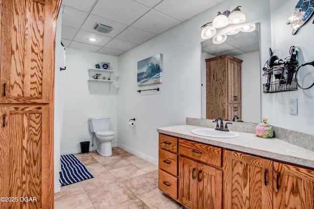 full bath with visible vents, baseboards, toilet, vanity, and a paneled ceiling