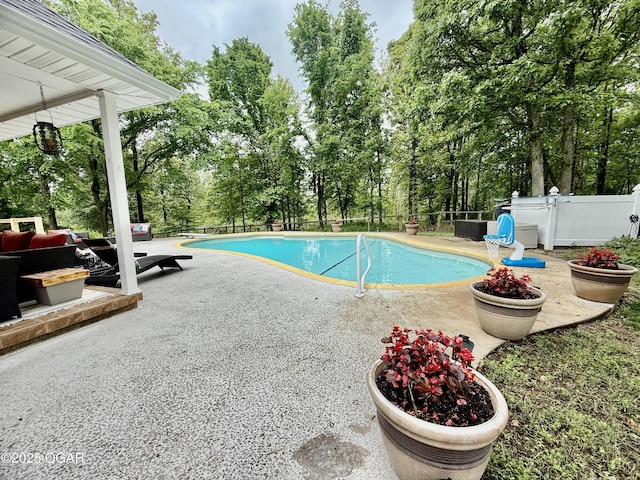 swimming pool with a patio area, fence, and view of scattered trees