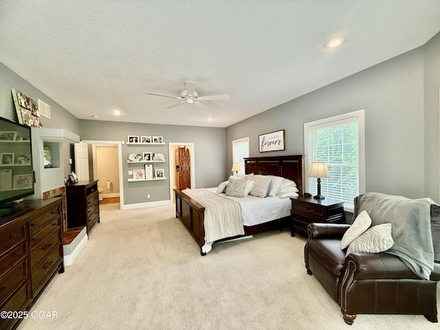 bedroom with light colored carpet, a textured ceiling, ensuite bath, a ceiling fan, and a walk in closet