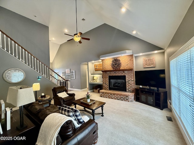 living area with a brick fireplace, stairs, high vaulted ceiling, ceiling fan, and carpet flooring