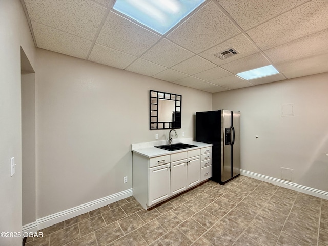 kitchen featuring a sink, a paneled ceiling, stainless steel refrigerator with ice dispenser, light countertops, and baseboards