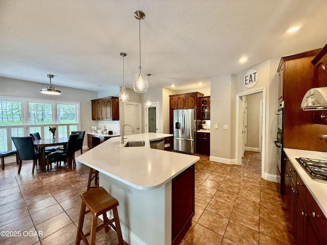 kitchen with appliances with stainless steel finishes, a sink, light countertops, an island with sink, and a breakfast bar