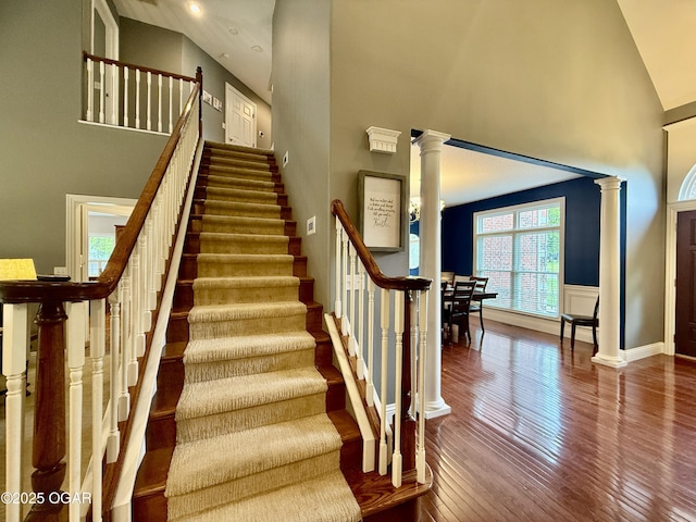 staircase featuring decorative columns, high vaulted ceiling, hardwood / wood-style flooring, and baseboards