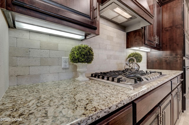 kitchen featuring dark brown cabinetry, premium range hood, light stone countertops, and stainless steel gas stovetop