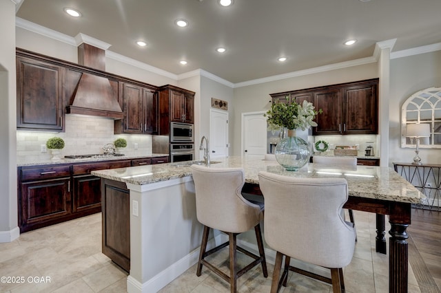 kitchen featuring a breakfast bar area, backsplash, a large island, a sink, and premium range hood