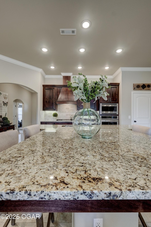 kitchen with visible vents, crown molding, light stone countertops, arched walkways, and appliances with stainless steel finishes