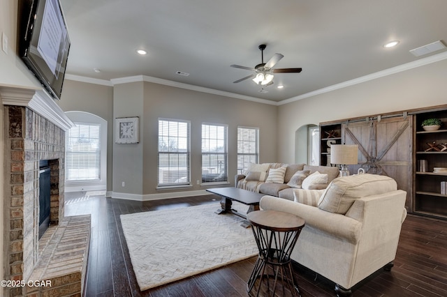living area with ceiling fan, visible vents, arched walkways, a brick fireplace, and dark wood finished floors