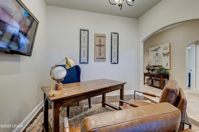 office area featuring baseboards, arched walkways, wood finished floors, and a notable chandelier