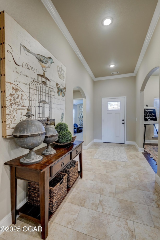entrance foyer featuring crown molding, arched walkways, baseboards, and visible vents