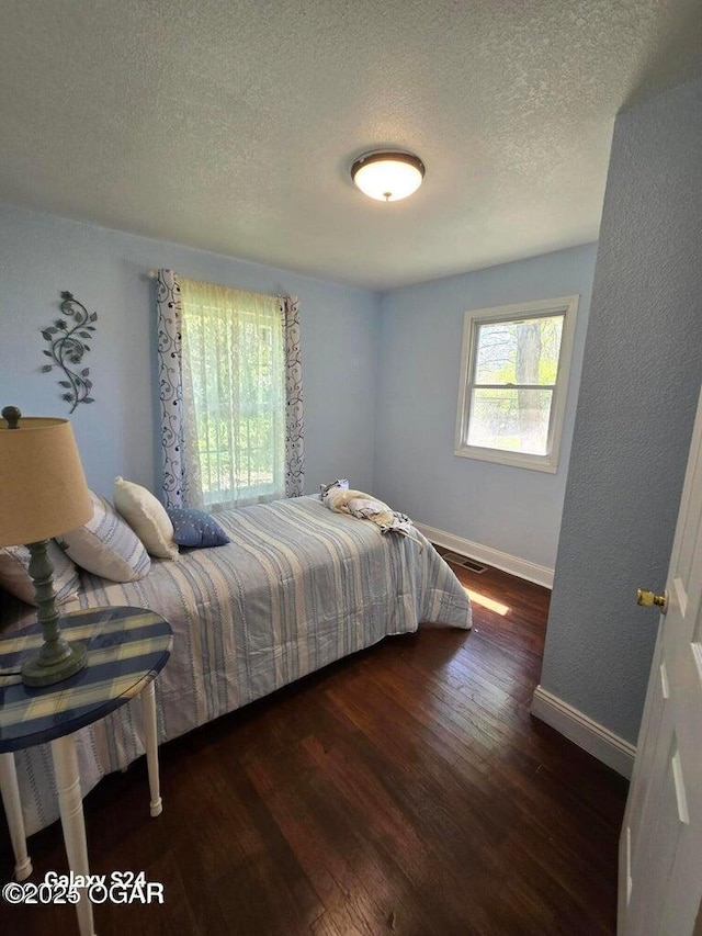 bedroom featuring dark wood finished floors, baseboards, visible vents, and a textured ceiling