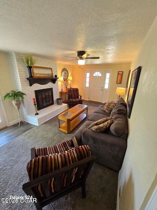 living room with a textured ceiling, ceiling fan, carpet flooring, and a brick fireplace