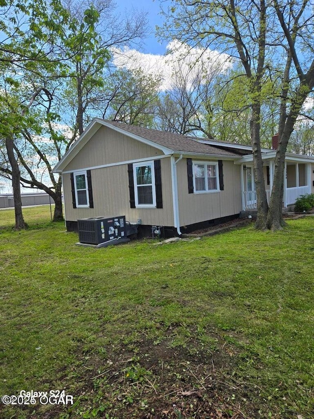 exterior space with cooling unit, a shingled roof, and a front lawn