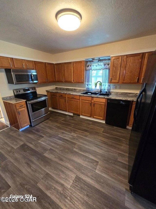kitchen with dark wood-type flooring, a textured ceiling, a sink, black appliances, and brown cabinetry