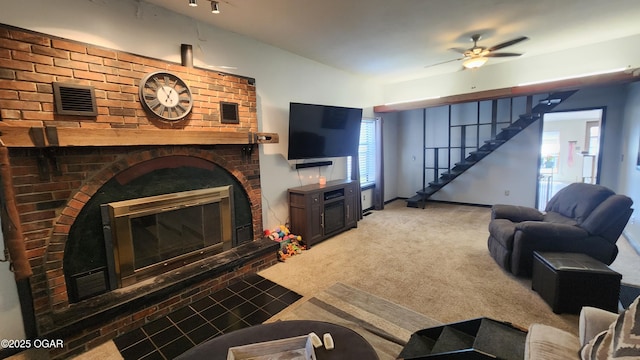 carpeted living room with stairs, a fireplace, visible vents, and a ceiling fan
