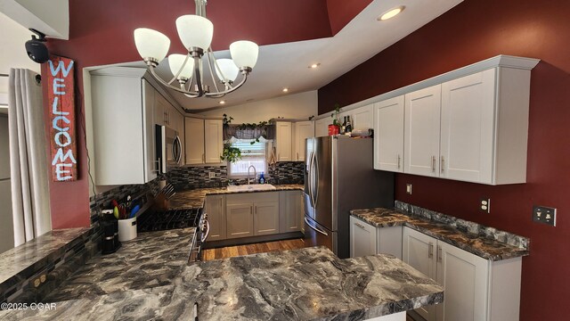 kitchen with lofted ceiling, an inviting chandelier, backsplash, a sink, and appliances with stainless steel finishes