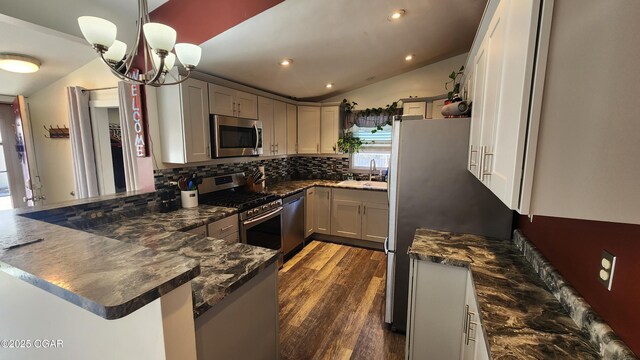 kitchen with tasteful backsplash, appliances with stainless steel finishes, a peninsula, dark wood-style floors, and lofted ceiling
