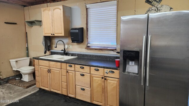 kitchen featuring concrete flooring, dark countertops, light brown cabinets, a sink, and stainless steel fridge with ice dispenser
