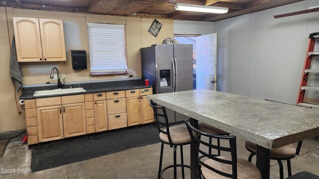kitchen featuring concrete floors, dark countertops, a sink, stainless steel refrigerator with ice dispenser, and light brown cabinetry